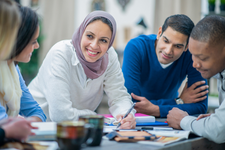 A Muslim woman wearing a hijab is leading a discussion meeting with her multi ethnic group of entrepreneurs in an office.