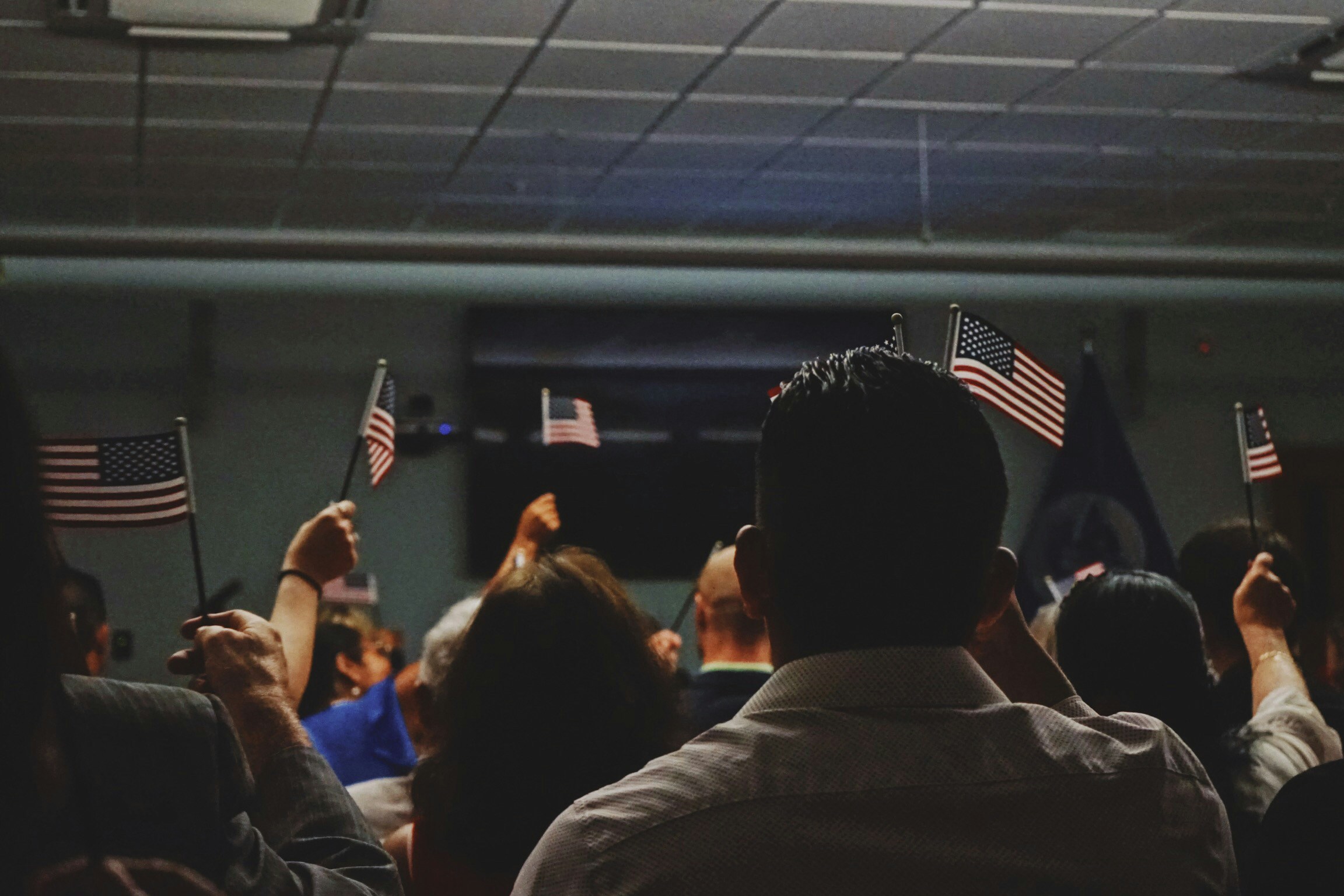Group of people waving small American flags at an indoor event.