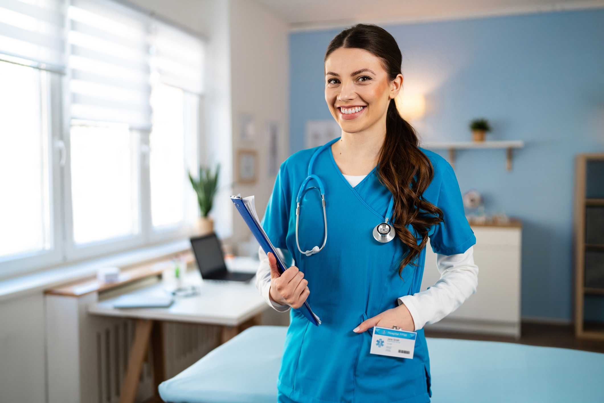 Portrait of young Caucasian female doctor or nurse in a blue medical scrub, holding a patient medical chart at the ordination