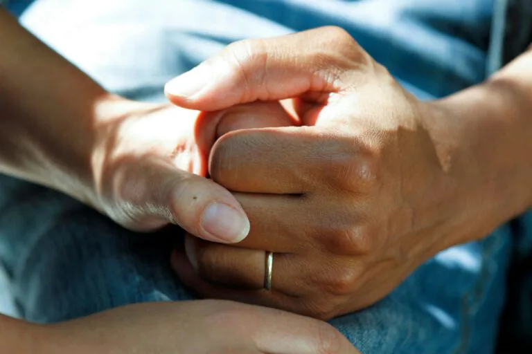 Close-up of two hands gently holding each other in comfort and support.