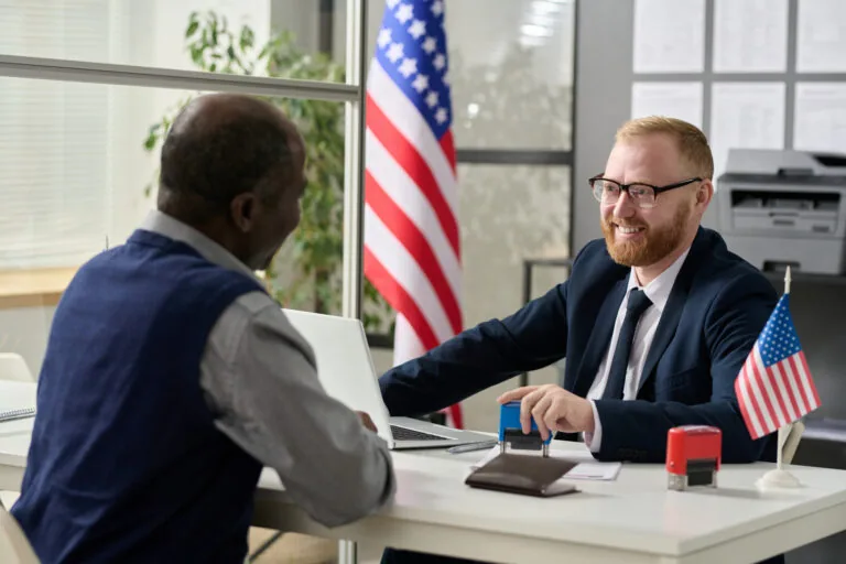 Portrait of friendly smiling worker consulting senior man in US immigration office