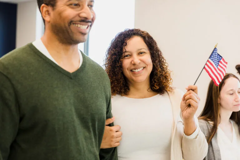 Smiling couple shows patriotism. Woman holds small flag. Casual attire.